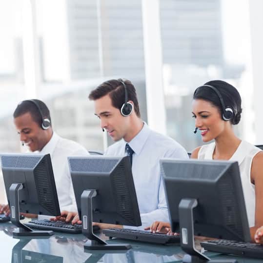 A group of people with headsets and computer answering phones in a call center located in a busy city.