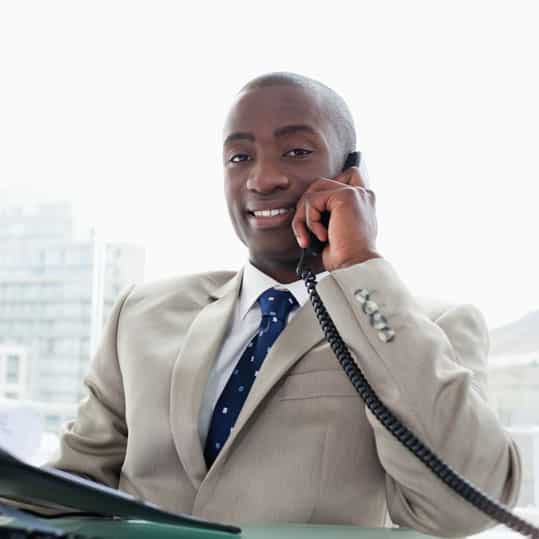 A dark handsome business owner is smiling while on the phone.