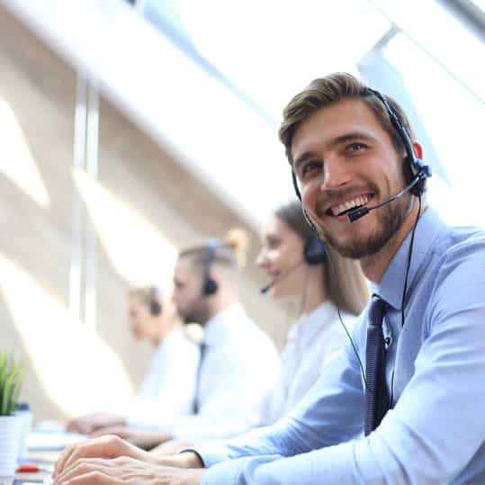 A Call center worker with a headset is accompanied by his colleagues busy answering the phone.