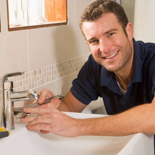 A Plumber working on a sink is smiling at the camera.